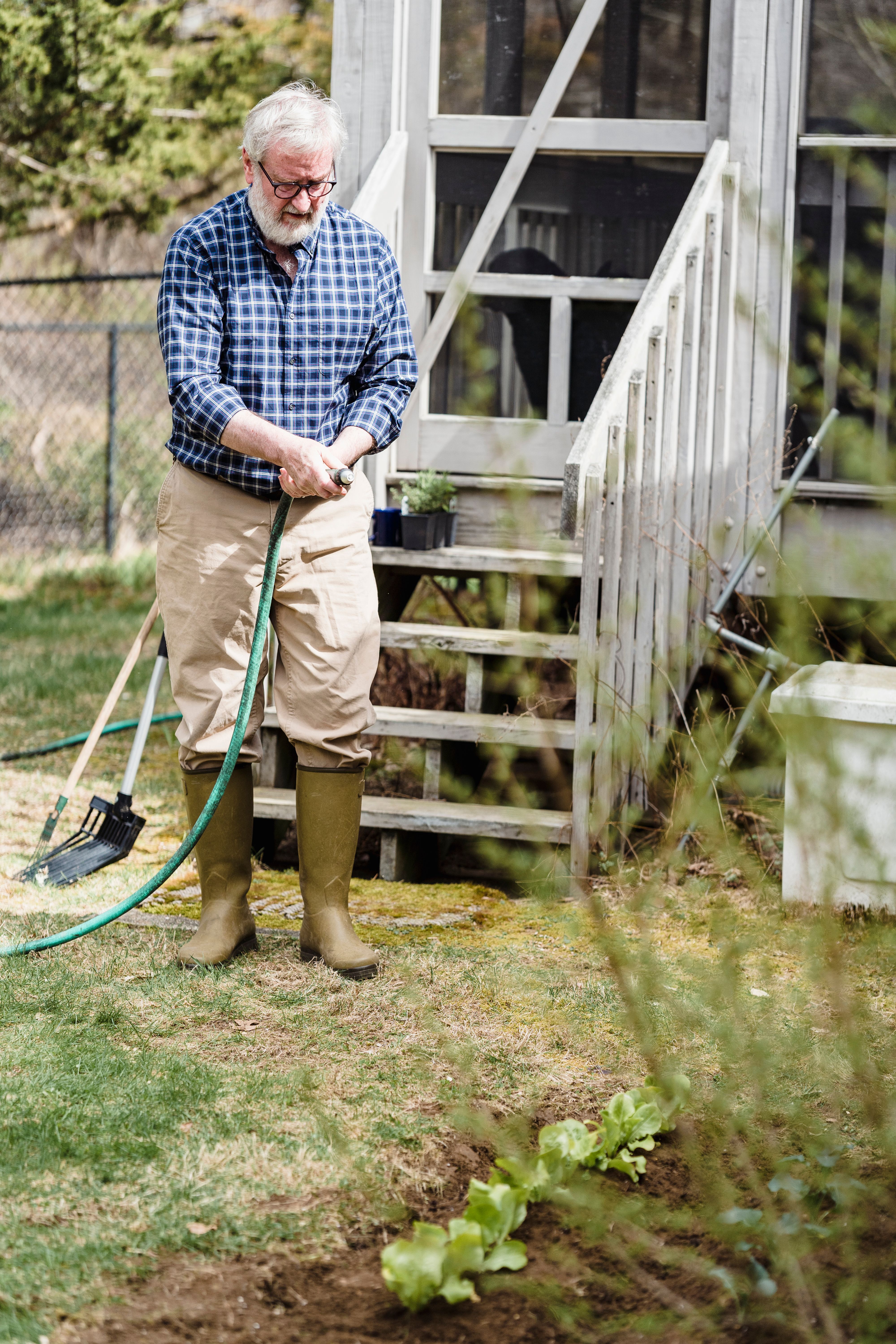 A gardener watering plants with a hose in a backyard